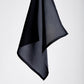 A single, suspended black cloth hangs against a plain gray background, conveying simplicity and elegance with its soft folds and flowing lines.