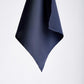 A dark navy blue handkerchief hangs against a plain white background, showcasing its smooth texture and elegant, folded edges. Simple and refined.